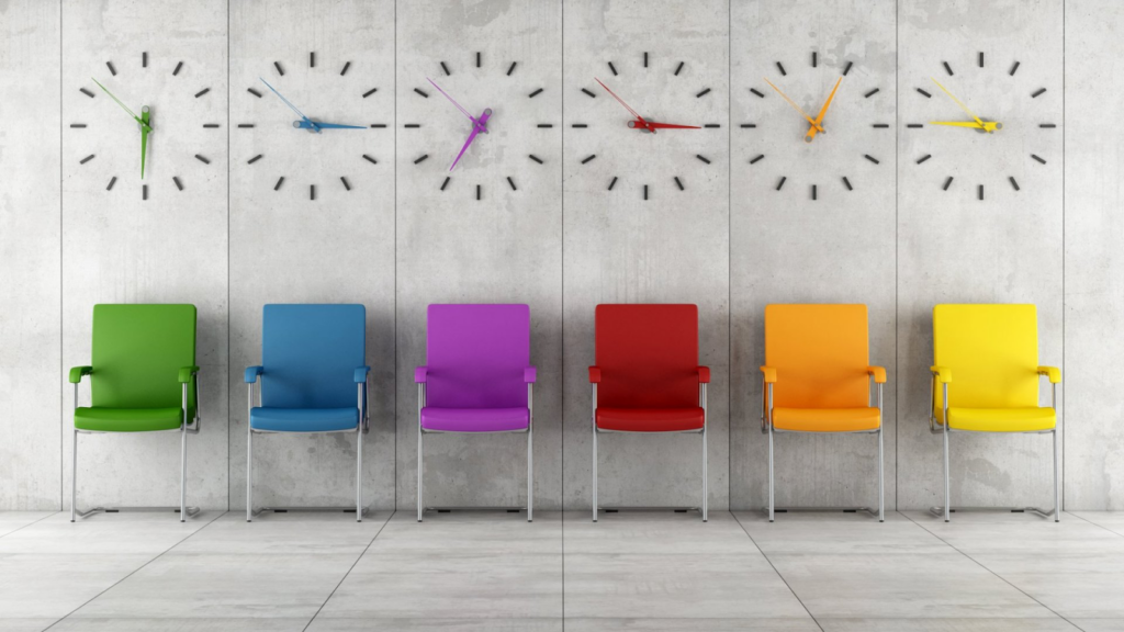 6 different colored chairs lined up on a wall with clocks above each chair.